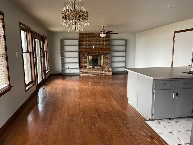 unfurnished living room featuring a fireplace, ceiling fan with notable chandelier, light hardwood / wood-style flooring, built in shelves, and brick wall