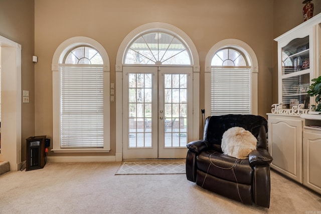 sitting room with a towering ceiling, light carpet, and french doors