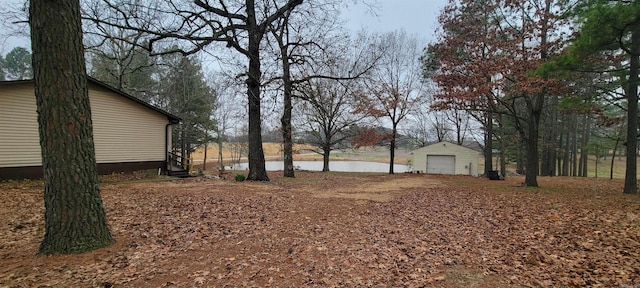 view of yard with a garage, a water view, and an outbuilding