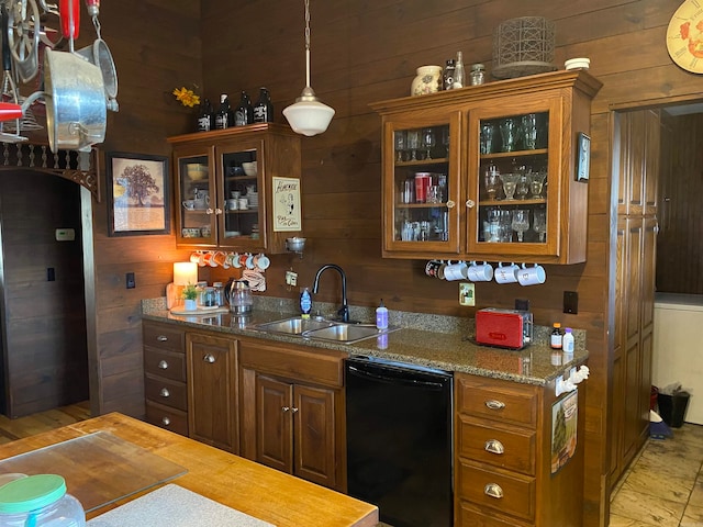 kitchen featuring wood walls, decorative light fixtures, dark stone counters, black dishwasher, and sink