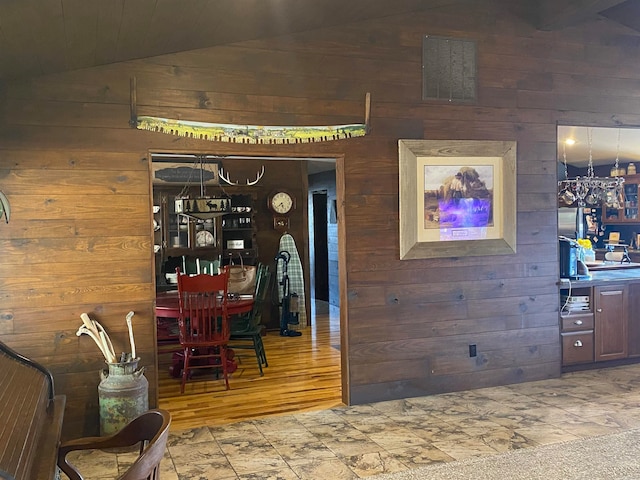 interior space with tile floors, wood walls, a chandelier, and lofted ceiling