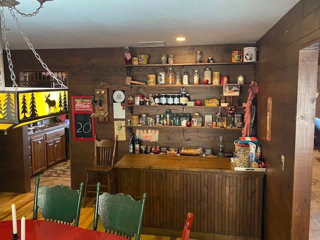 bar featuring wooden walls, dark brown cabinets, and light wood-type flooring