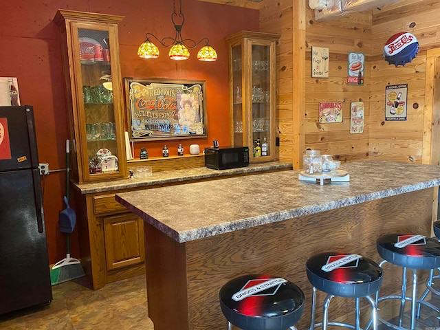 kitchen with wooden walls, black appliances, a breakfast bar area, and pendant lighting