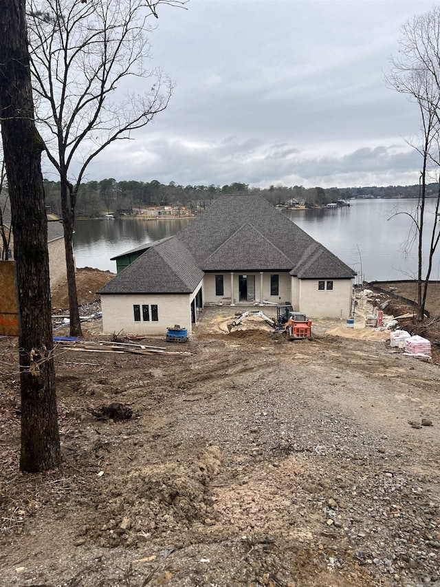 back of house with a water view, driveway, and a shingled roof