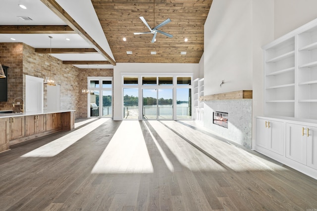 unfurnished living room featuring built in shelves, a towering ceiling, a glass covered fireplace, wood finished floors, and beamed ceiling