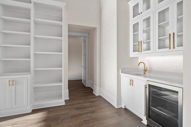 bar with beverage cooler, dark wood-type flooring, a sink, baseboards, and wet bar