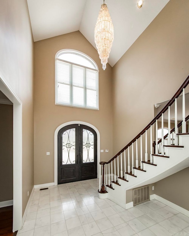 tiled entrance foyer with a notable chandelier, high vaulted ceiling, and french doors