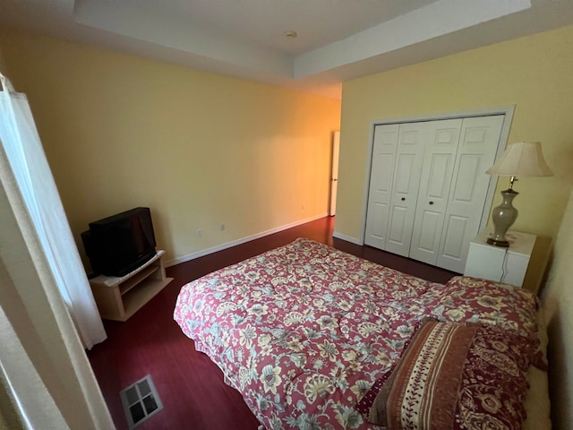 bedroom with a raised ceiling, dark hardwood / wood-style floors, and a closet