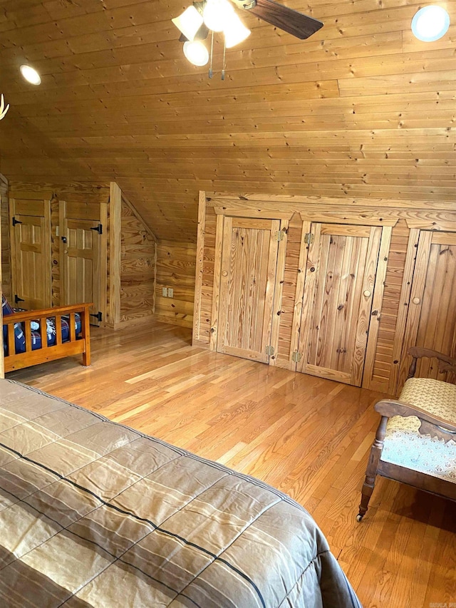 bedroom with ceiling fan, lofted ceiling, wood ceiling, wood walls, and light wood-type flooring