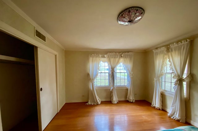 unfurnished bedroom featuring light hardwood / wood-style flooring, ornamental molding, a closet, and multiple windows