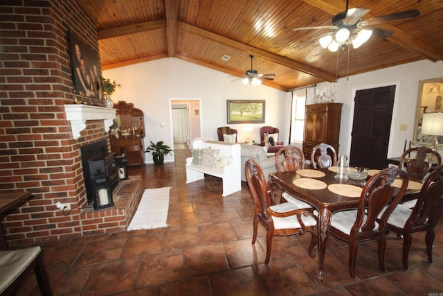 dining room with vaulted ceiling with beams, a wood stove, a fireplace, ceiling fan, and dark tile flooring