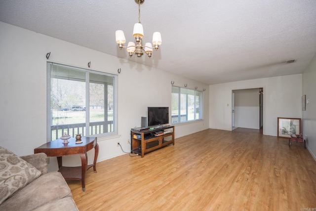 living room with light hardwood / wood-style floors, a textured ceiling, and a notable chandelier