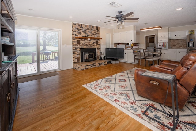 living room featuring a fireplace, crown molding, ceiling fan, and light wood-type flooring