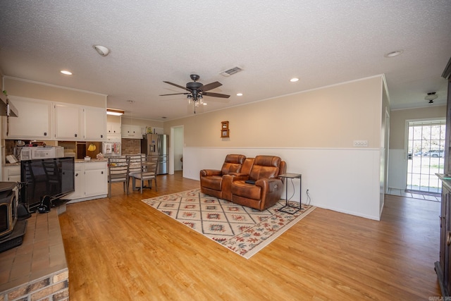 living room with ceiling fan, a textured ceiling, ornamental molding, and light hardwood / wood-style floors