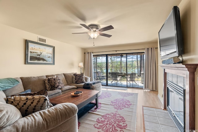 living room with ceiling fan, a tile fireplace, and light hardwood / wood-style floors