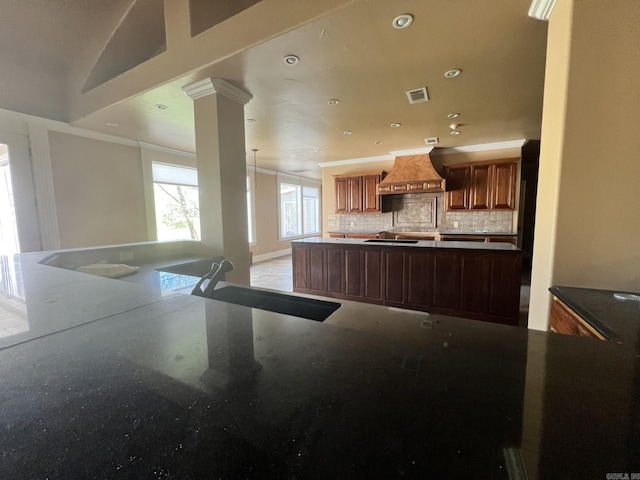 kitchen with backsplash, custom exhaust hood, decorative columns, and dark stone countertops