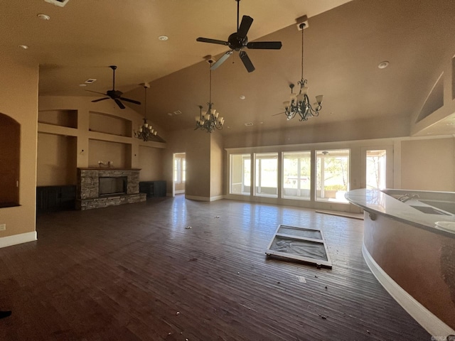 unfurnished living room with a stone fireplace, high vaulted ceiling, dark hardwood / wood-style floors, and ceiling fan with notable chandelier