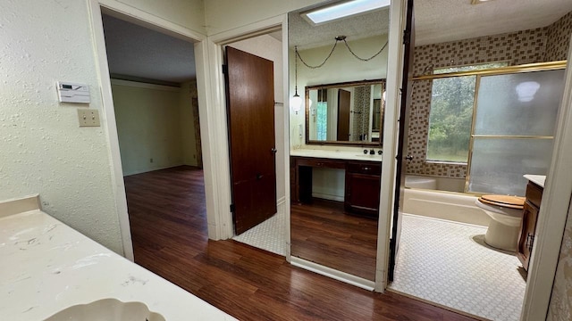 full bathroom featuring toilet, a textured ceiling, vanity, enclosed tub / shower combo, and hardwood / wood-style floors