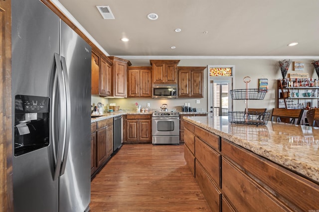 kitchen with light stone countertops, hardwood / wood-style floors, appliances with stainless steel finishes, crown molding, and a breakfast bar area