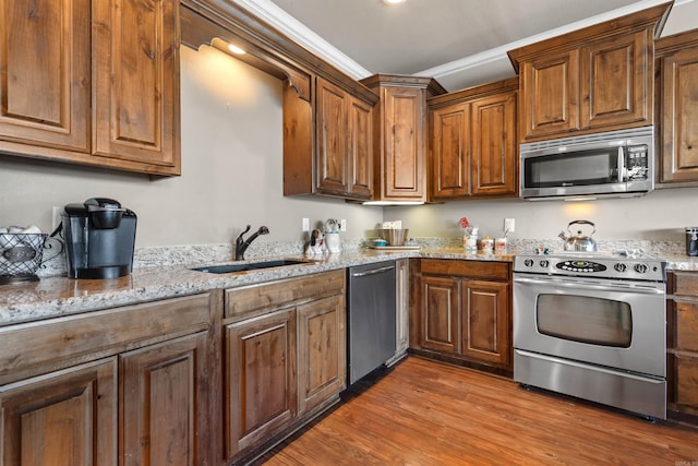 kitchen with light hardwood / wood-style floors, crown molding, stainless steel appliances, light stone countertops, and sink