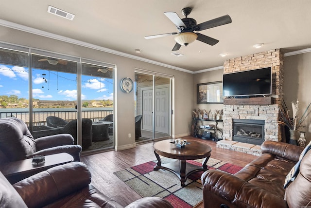 living room featuring ceiling fan, ornamental molding, a stone fireplace, and dark hardwood / wood-style floors