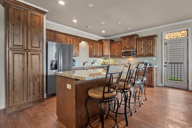 kitchen featuring stainless steel appliances, a kitchen island, light stone countertops, a breakfast bar area, and dark hardwood / wood-style flooring