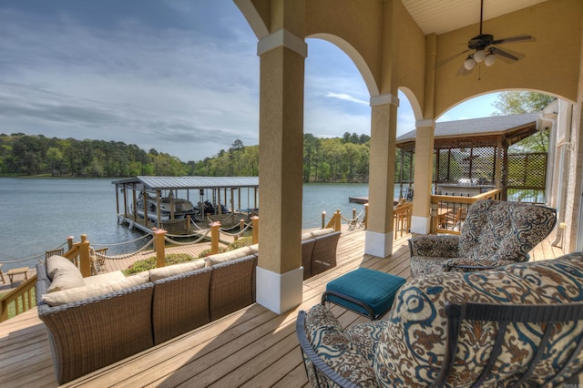 wooden terrace featuring an outdoor living space, ceiling fan, a dock, and a water view