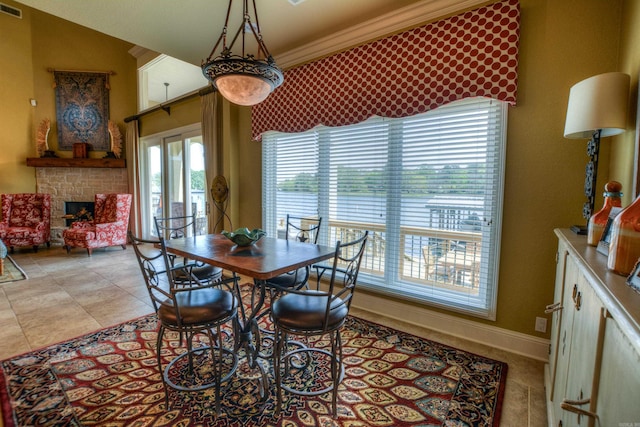 dining area with light tile floors, a stone fireplace, and ornamental molding