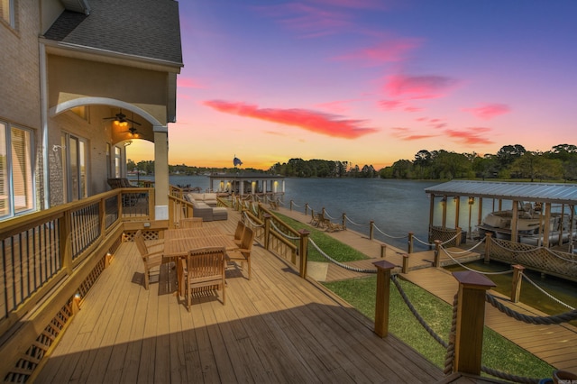 deck at dusk featuring a water view and a dock