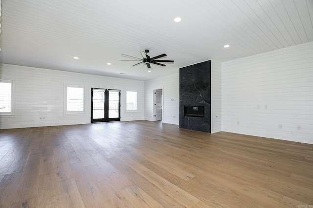 unfurnished living room featuring ceiling fan, a wealth of natural light, dark wood-type flooring, and a large fireplace