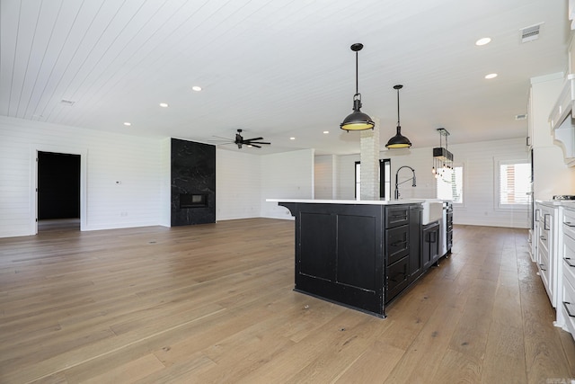 kitchen featuring light hardwood / wood-style flooring, pendant lighting, a kitchen island with sink, and white cabinets