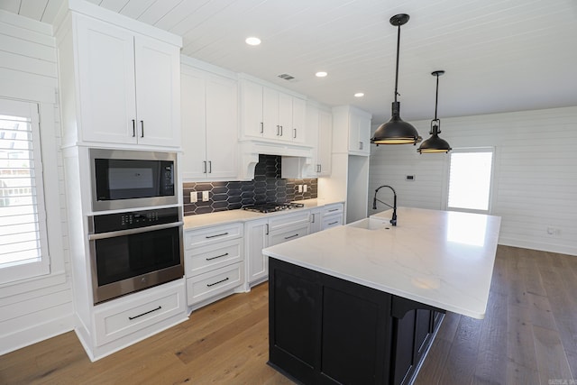 kitchen with appliances with stainless steel finishes, sink, light hardwood / wood-style flooring, a kitchen island with sink, and hanging light fixtures