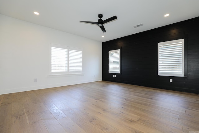 empty room with wooden walls, light hardwood / wood-style floors, and ceiling fan