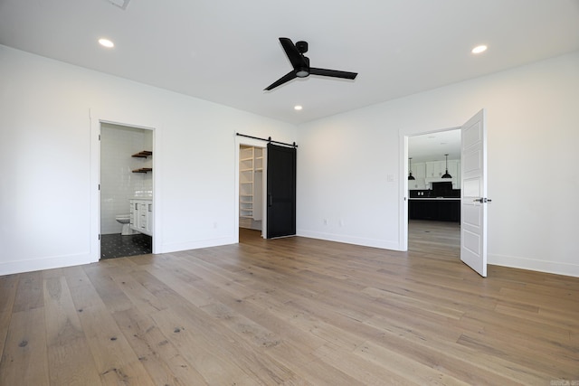 unfurnished bedroom featuring light hardwood / wood-style floors, ensuite bathroom, a walk in closet, and a barn door