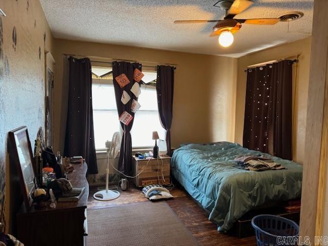 bedroom with dark hardwood / wood-style floors, ceiling fan, and a textured ceiling