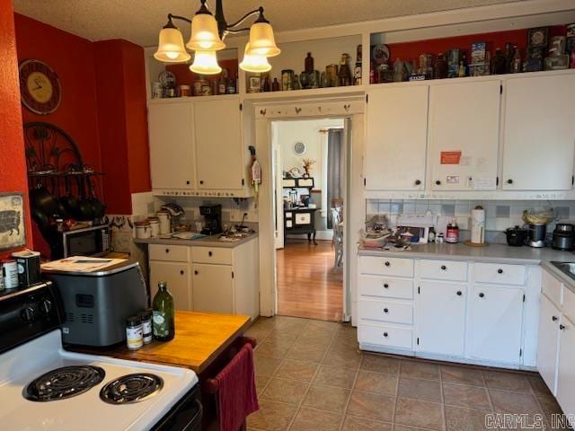 kitchen with white cabinetry, decorative light fixtures, backsplash, range, and a notable chandelier