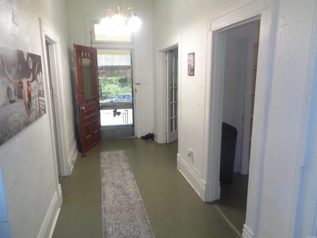 hallway with a notable chandelier, baseboards, and concrete flooring