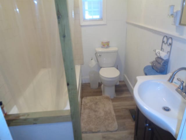 bathroom featuring toilet, wood finished floors, vanity, and shower / bathtub combination with curtain