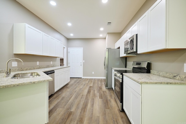 kitchen with stainless steel appliances, sink, white cabinetry, light stone counters, and light wood-type flooring