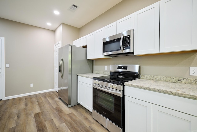 kitchen featuring stainless steel appliances, light stone counters, white cabinets, and light hardwood / wood-style floors