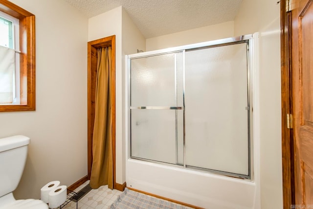 bathroom with combined bath / shower with glass door, tile patterned floors, a textured ceiling, and toilet