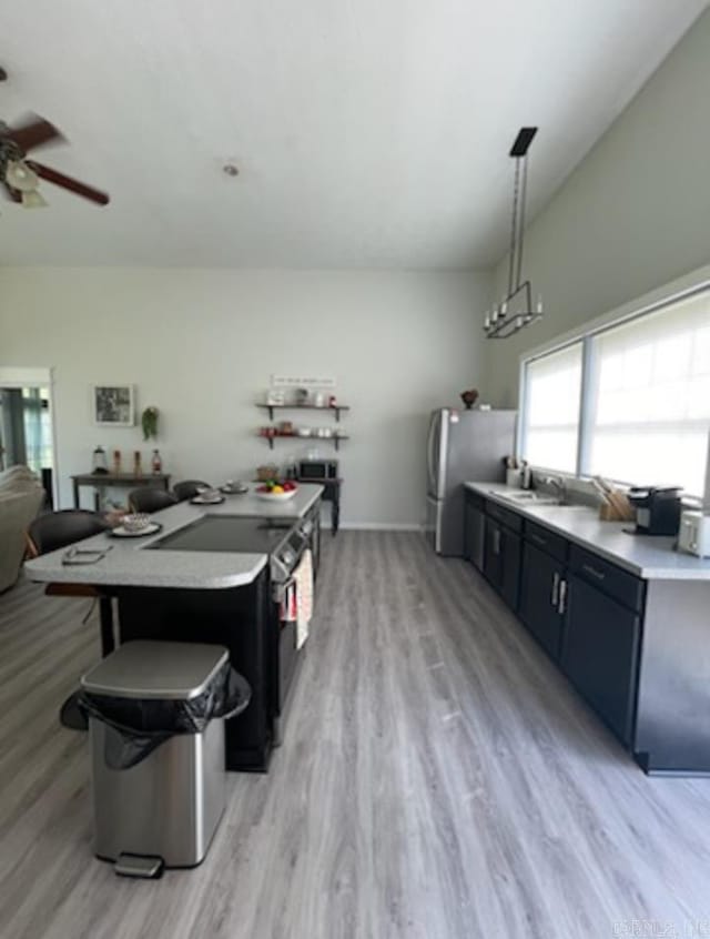 kitchen featuring decorative light fixtures, appliances with stainless steel finishes, a breakfast bar area, ceiling fan, and light wood-type flooring