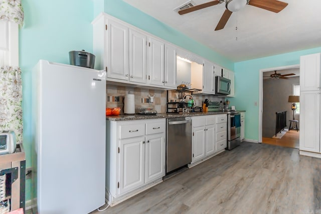 kitchen with light wood-type flooring, white cabinetry, backsplash, stainless steel appliances, and ceiling fan