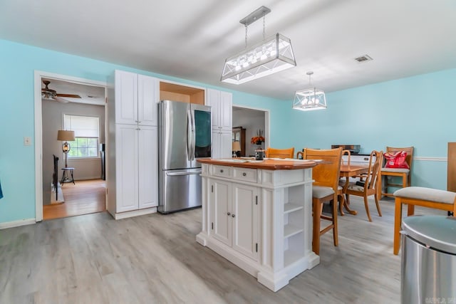 kitchen featuring hanging light fixtures, white cabinets, stainless steel refrigerator, ceiling fan with notable chandelier, and light hardwood / wood-style floors