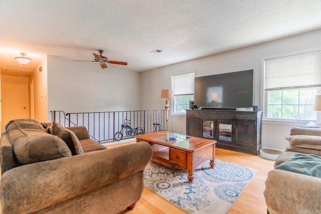 living room with a textured ceiling, ceiling fan, and light wood-type flooring