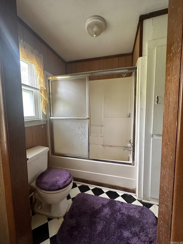 bathroom featuring wooden walls, tile floors, combined bath / shower with glass door, toilet, and a textured ceiling