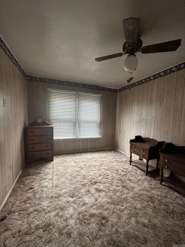 misc room with a textured ceiling, ceiling fan, wooden walls, and dark colored carpet