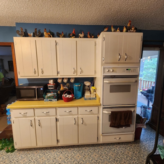 kitchen featuring a textured ceiling, double oven, and white cabinetry