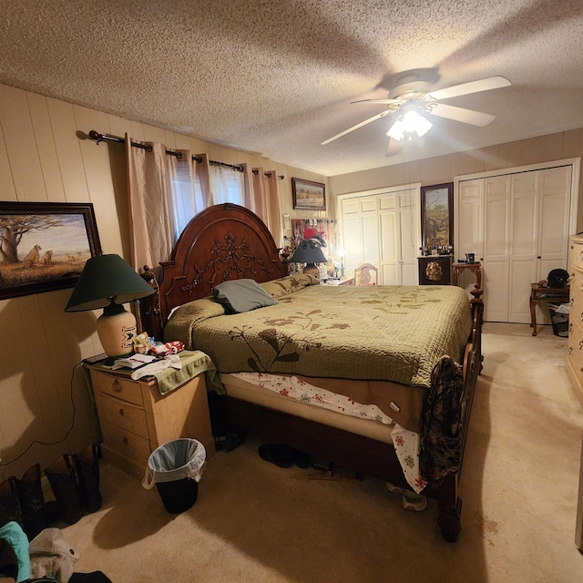 bedroom featuring light carpet, ceiling fan, a textured ceiling, and multiple closets