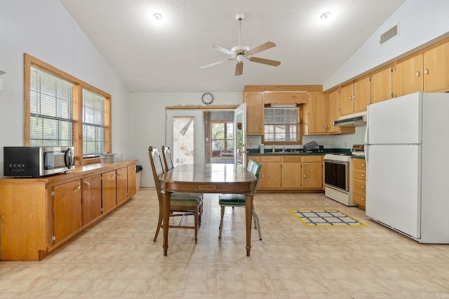 kitchen featuring ceiling fan, light tile flooring, stove, lofted ceiling, and white refrigerator